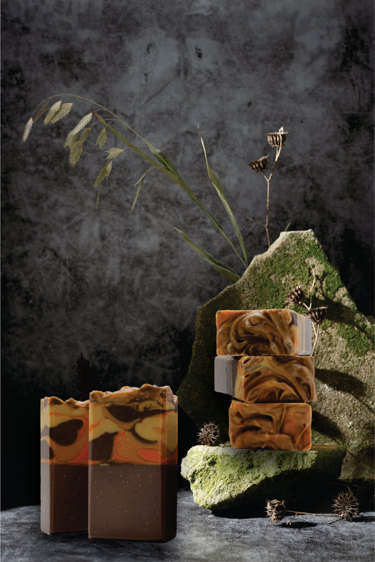 Three bars of soap with a natural, earthy design on a dark background with greenery.