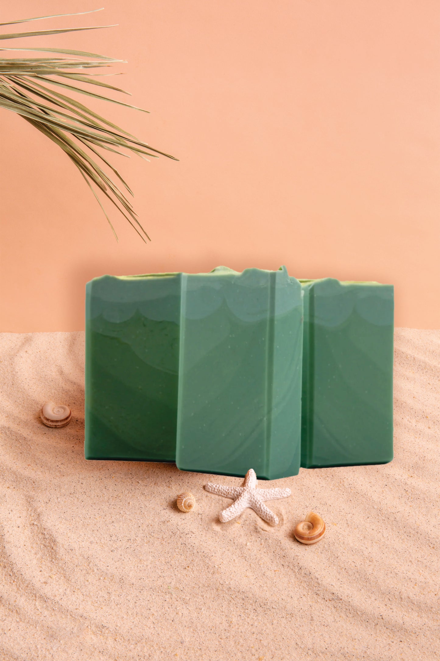 Three green rectangular objects on sand with a starfish and seashells, against a peach-colored background.