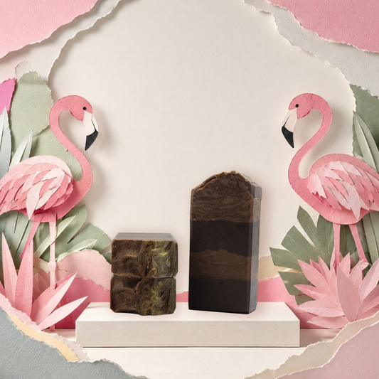 Two rectangular artisan soap bars displayed on a white pedestal. One bar is dark brown with natural stone-like marbling, and the other is a layered dark brown and black soap bar.