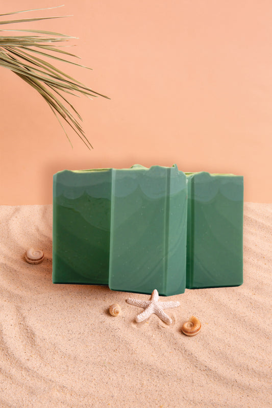 Three green rectangular objects on sand with a starfish and seashells, against a peach-colored background.