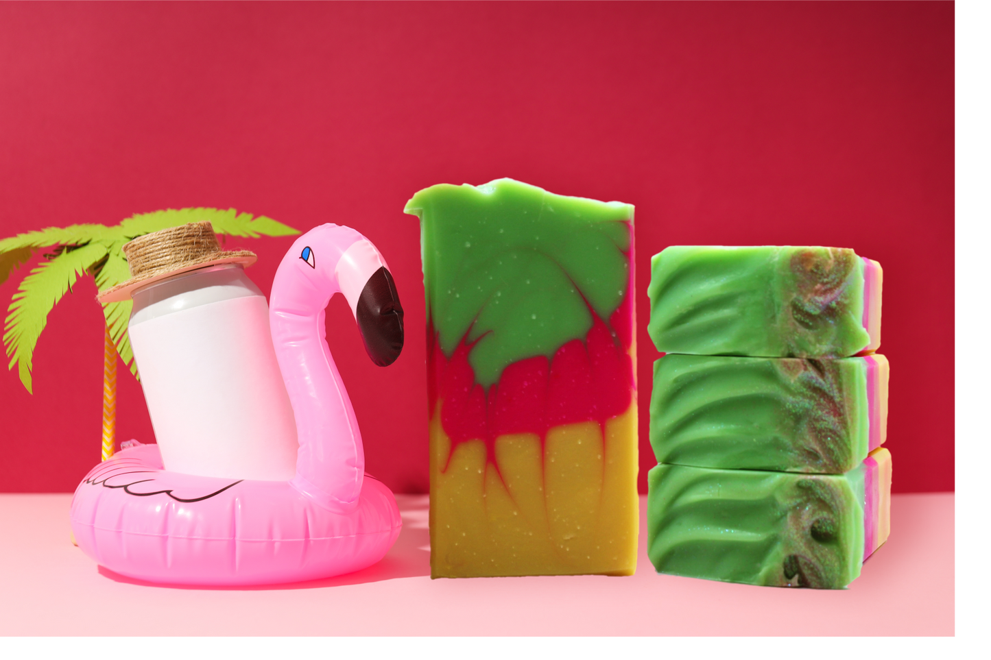 Three colorful soap bars with a pink flamingo float and palm leaf on a red background