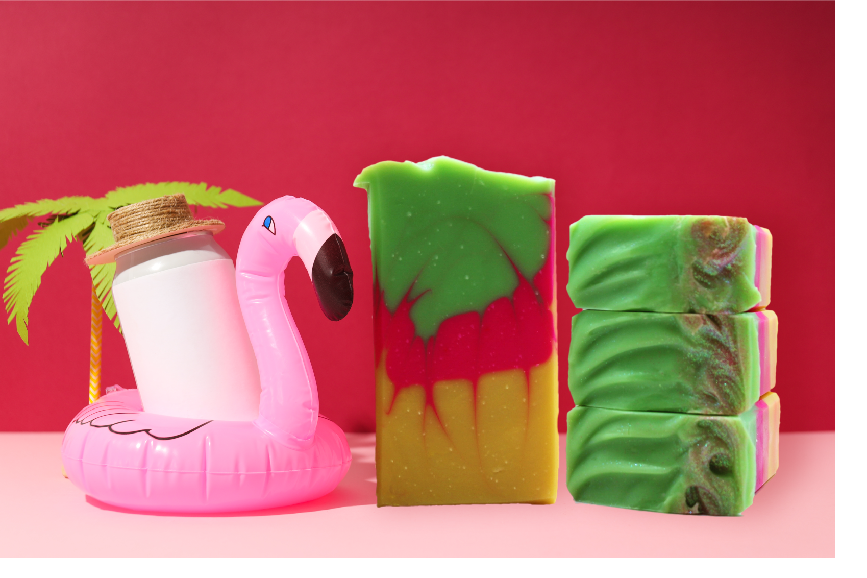 Three colorful soap bars with a pink flamingo float and palm leaf on a red background